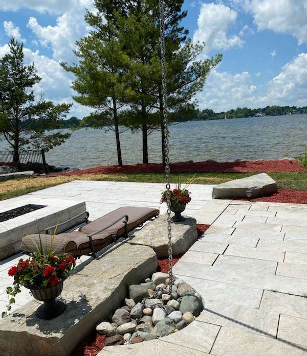 Stone paving, flowering planters and a rock bed beside a lake