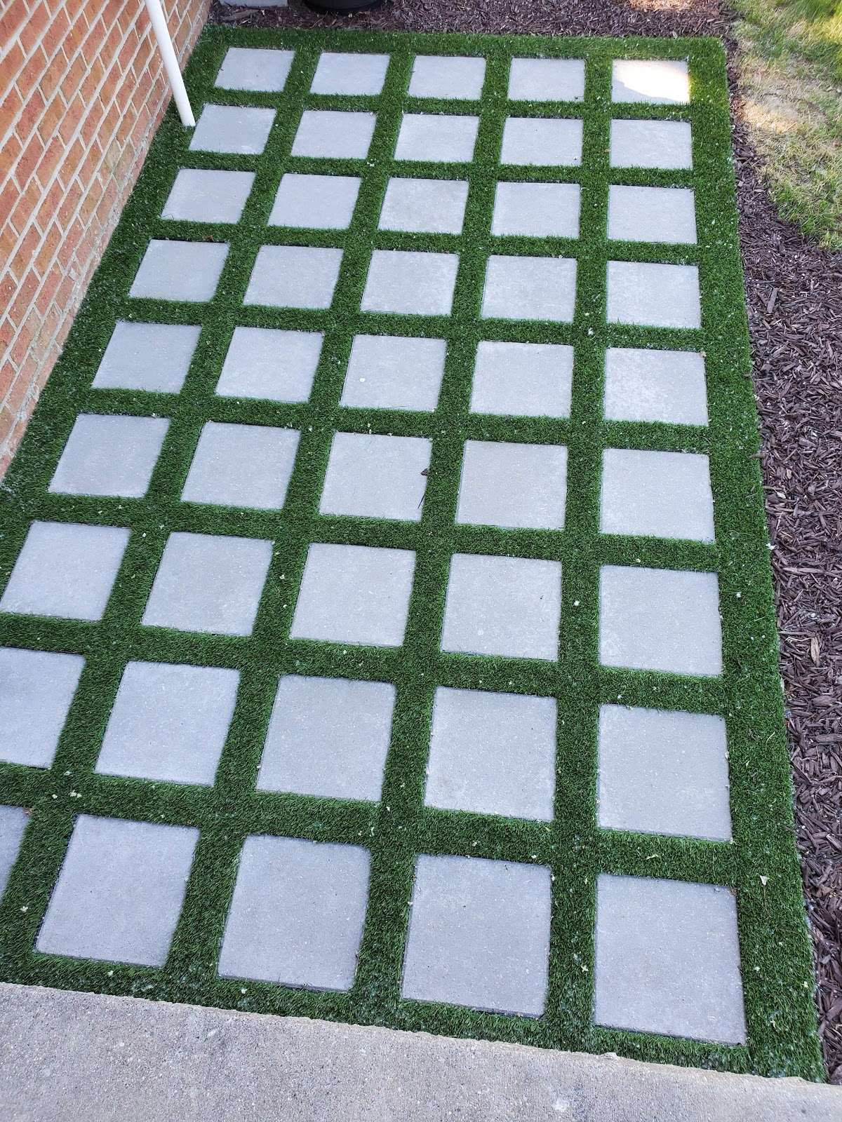 Square pale pavers set in a green grid beside a brick wall
